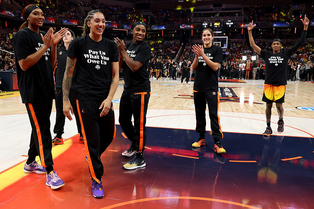 Kiki Iriafen #44 of the Washington Mystics, Gabby Williams #5 of the Seattle Storm, Jackie Young #0 of the Las Vegas Aces, Sonia Citron #2 of the Washington Mystics and Brittney Sykes #15 of the Washington Mystics wear shirts saying "Pay us what you owe us" prior to the 2025 AT&T WNBA All-Star Game at Gainbridge Fieldhouse on July 19, 2025 in Indianapolis, Indiana.